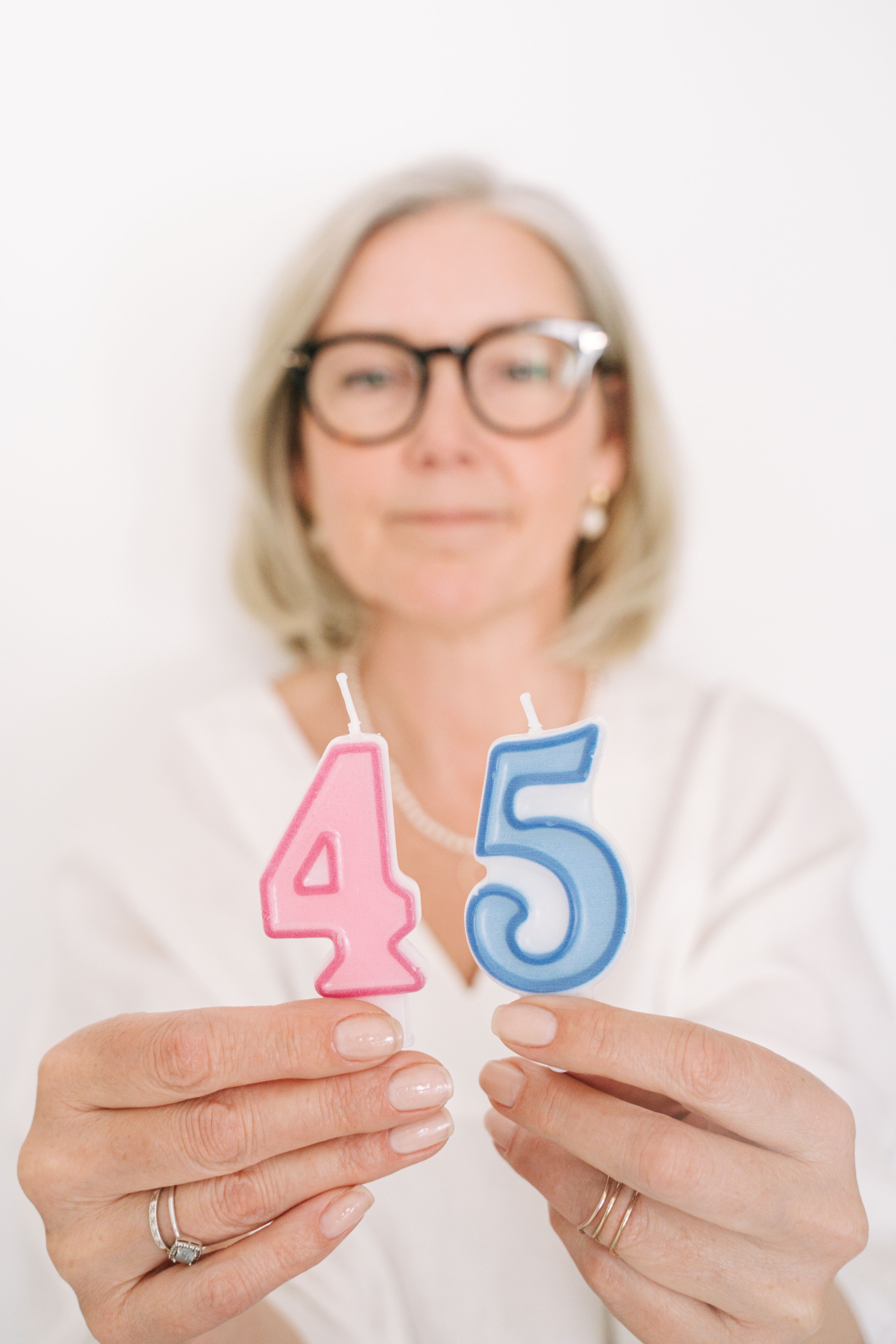 Frau um die 45 hält zwei Geburtstagskerzen mit den Zahlen 4 und 5 in den Händen